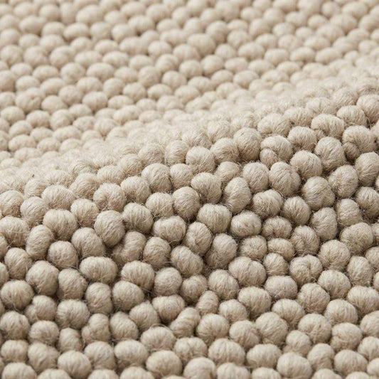 Chunky loop textured neutral area rug with braided edges in a modern organic interior setting