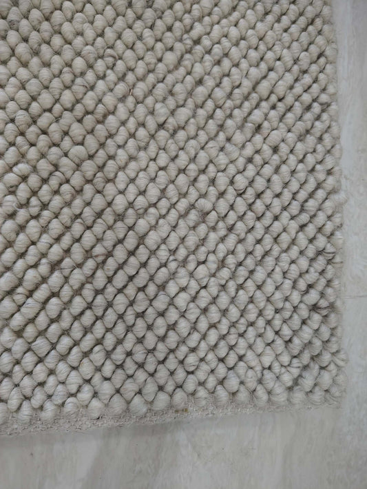 Chunky looped ivory rug with thick textured yarn and neutral minimalist design on hardwood floor