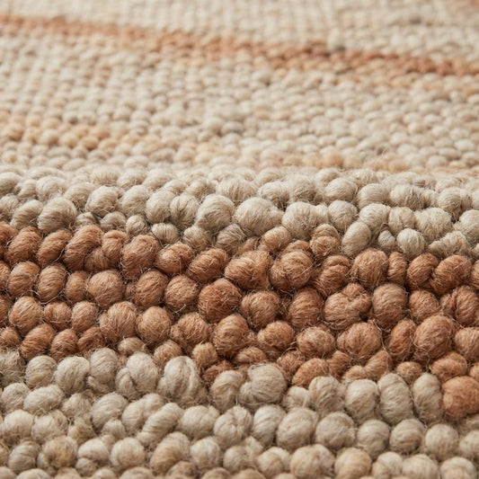 Close-up of thick pebble-textured wool rug with warm earthy stripe detail