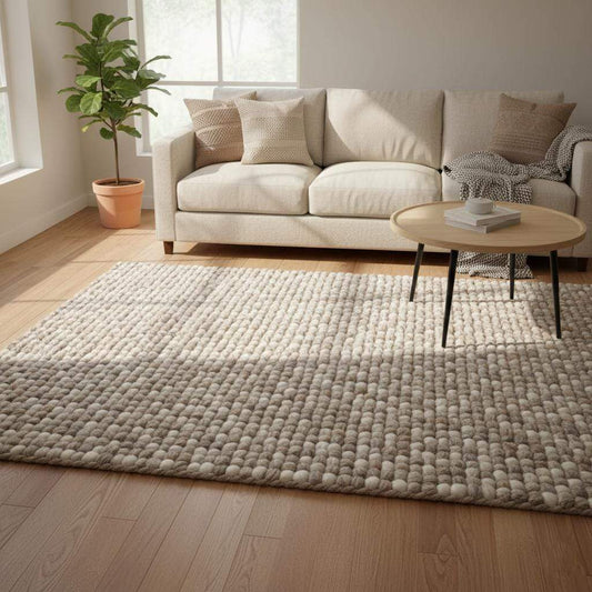 Handwoven chunky wool rug in neutral cream and beige tones with thick felted texture laying on wooden floor.