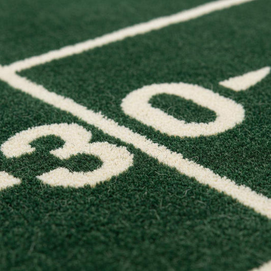 Close-up of plush green rug showing dense cut pile texture, clean white yard lines, and smooth fiber finish.