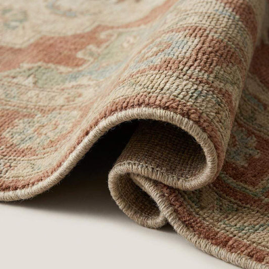Close up detail of hand knotted wool pile showing individual knots, muted yarn colors, and soft texture without latex backing.