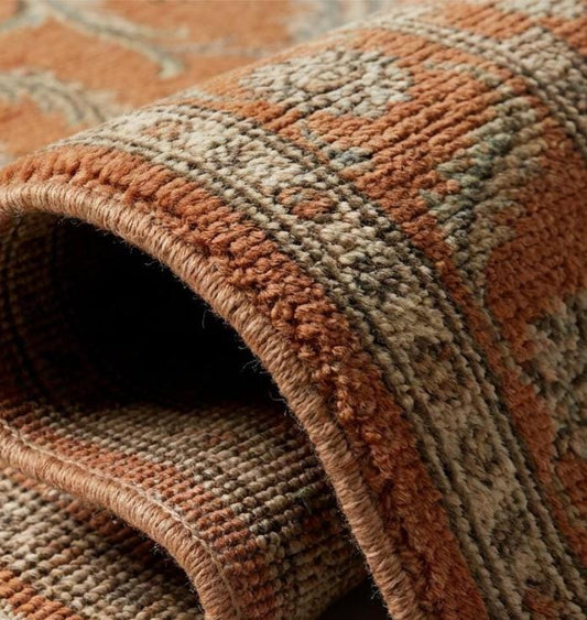 Close-up texture of a hand-knotted wool rug showing individual knot structure, low pile height, and intricate cream and olive green floral weaving.