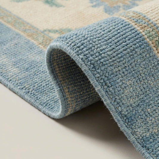 Close up of hand knotted wool rug showing individually tied knots, dense wool pile, and soft blue border fibers