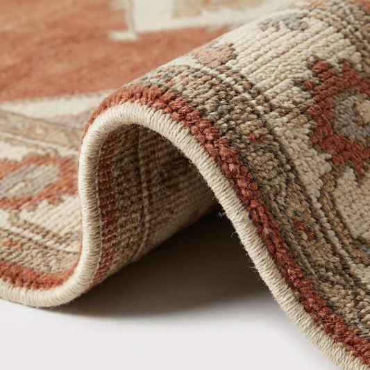 Close up of hand knotted wool pile texture showing individual knots, rich terracotta dye variation, and durable cotton fringe detail.