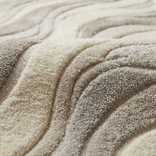 Close-up of carved high-low hand tufted wool pile showing soft dense fibers and sculpted wave texture.