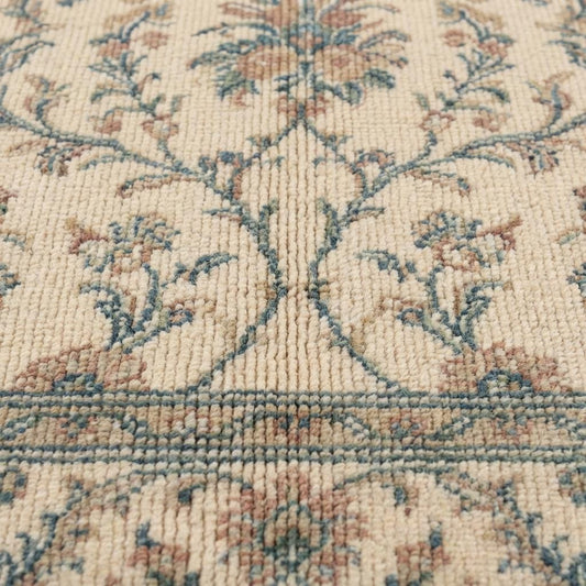 Close-up of hand knotted wool pile showing individual knot texture, dense ivory yarn, and detailed floral pattern