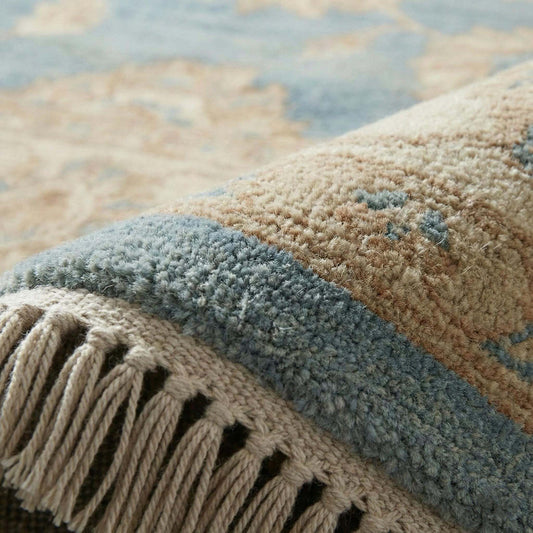 Oushak style hand knotted wool area rug with soft blue floral design and ivory border