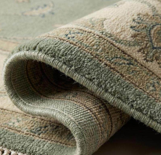 Sage green hand knotted Oushak rug with muted floral motifs and wool texture in living room setting
