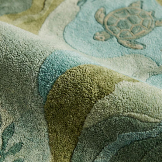 Close-up of tufted sea turtle rug texture showing carved wavy edges, plush fibers, and raised aquatic pattern in soft green and blue tones.