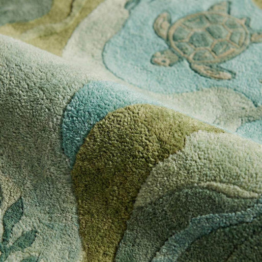Close-up of tufted sea turtle rug texture showing carved wavy edges, plush fibers, and raised aquatic pattern in soft green and blue tones.