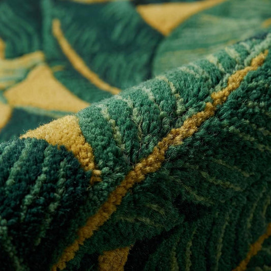 Close-up of sculpted tropical leaf rug showing high-pile tufted texture, carved green foliage detailing, and rich mustard background, highlighting plush fibers and dimensional craftsmanship.