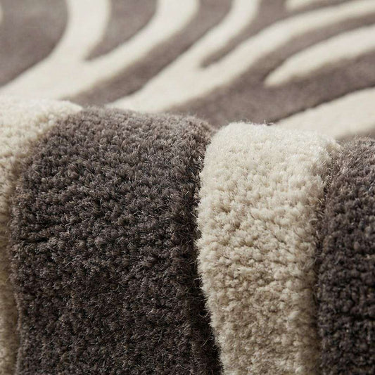 Close-up of hand tufted wool fibers showing raised carved zebra stripes, plush pile texture, and dense wool surface in ivory and charcoal tones.