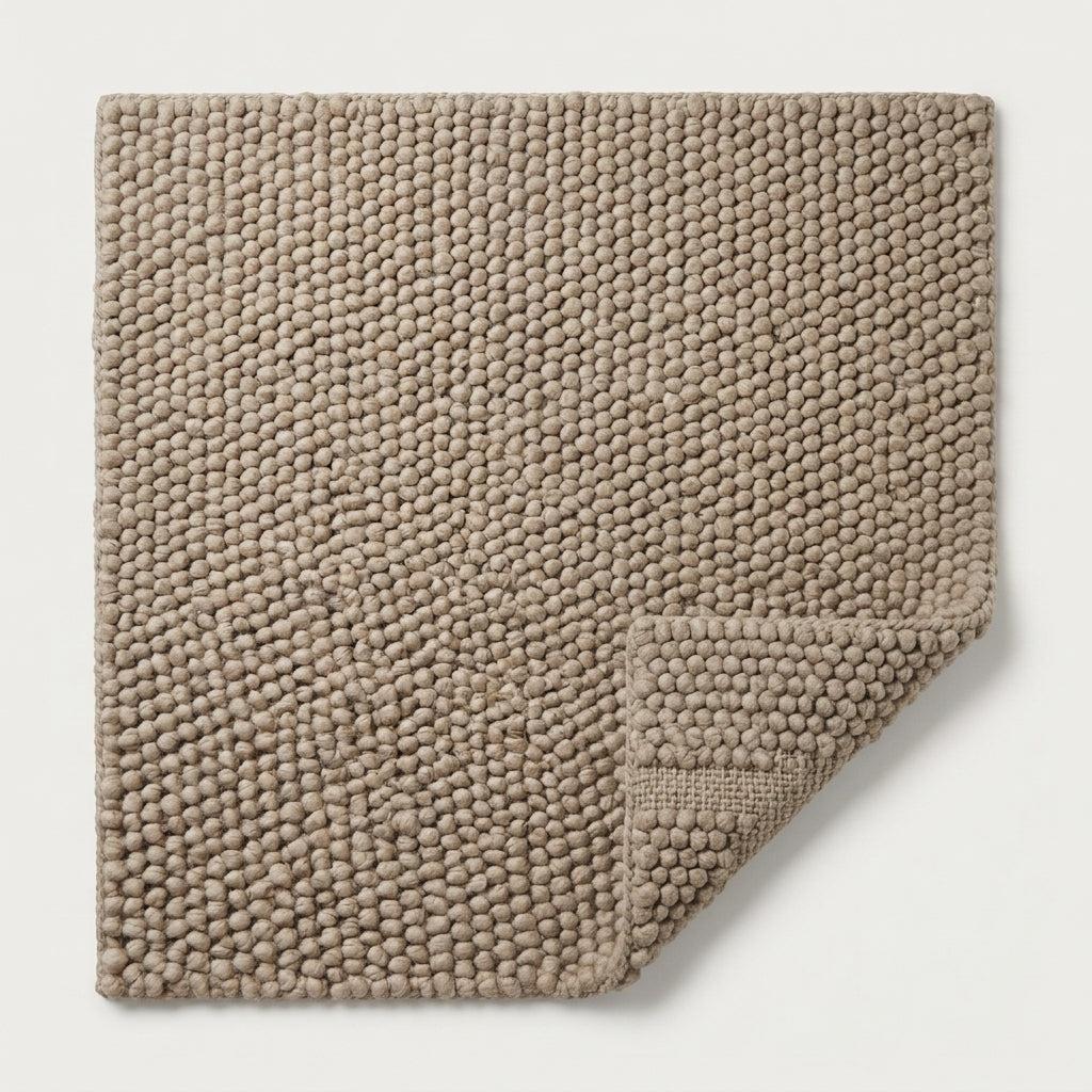 Chunky Wool Rug in warm taupe greige, with a thick handwoven pebble texture and a folded corner showing its backing.