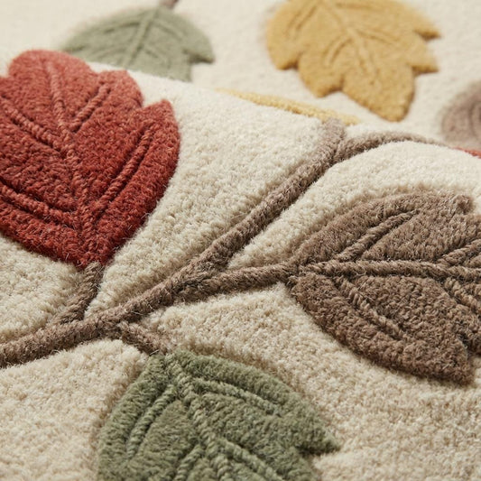 Close-up of textured botanical wool rug showing raised carved leaf design in terracotta, mustard, sage, and taupe on soft ivory background with plush pile detail.