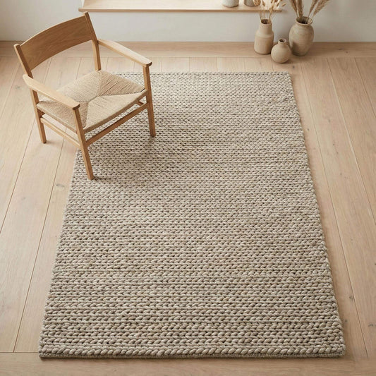 Chunky braided knit rug in neutral beige with thick textured yarn for cozy Nordic interiors