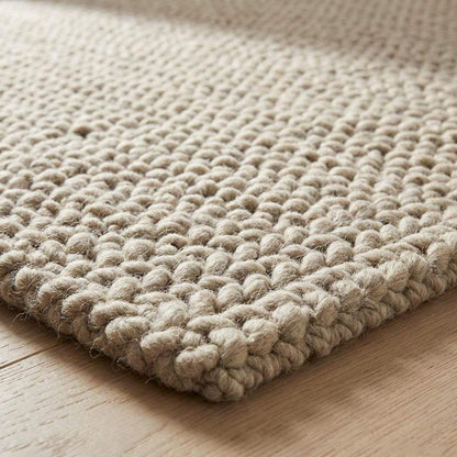 Chunky braided knit rug in neutral beige with thick textured yarn ideal for cozy Nordic interiors