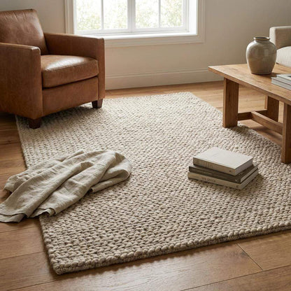 Chunky braided knit rug in neutral beige with thick textured yarn for cozy Nordic interiors