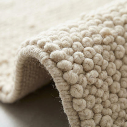 Ivory chunky knit wool rug with thick braided texture and soft hand-knit fibers for cozy neutral decor