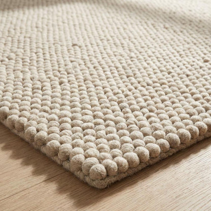 Chunky loop textured area rug in neutral cream with thick, nubby yarn and plush pebble-like surface in modern cozy living room setting