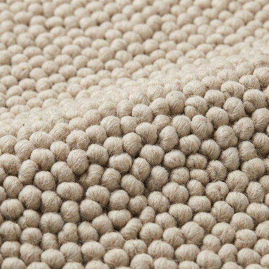 Chunky loop textured neutral area rug with braided edges in a modern organic interior setting