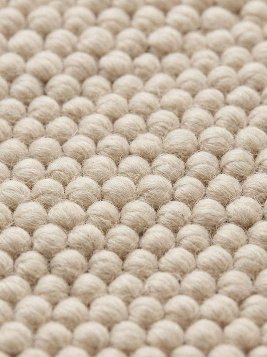 Detailed macro of dense loop weave and braided rug edge in neutral tone