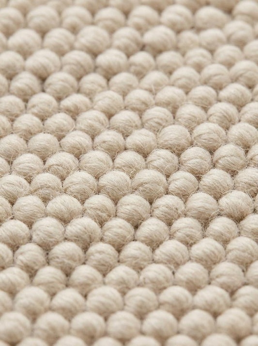 Detailed macro of dense loop weave and braided rug edge in neutral tone