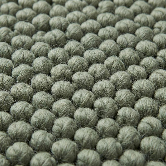 Close up of thick loop yarn texture on sage green minimalist rug