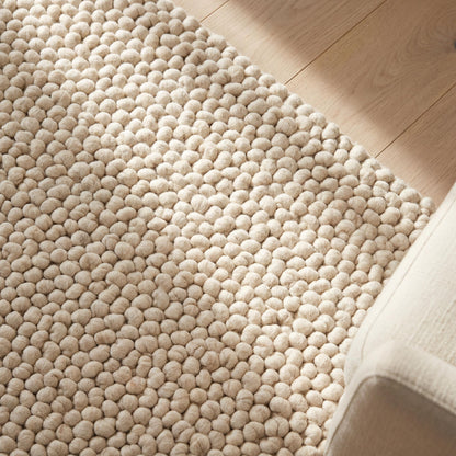 Handmade chunky wool pom pom rug in neutral tones, soft textured area rug for cozy boho nursery and living room decor