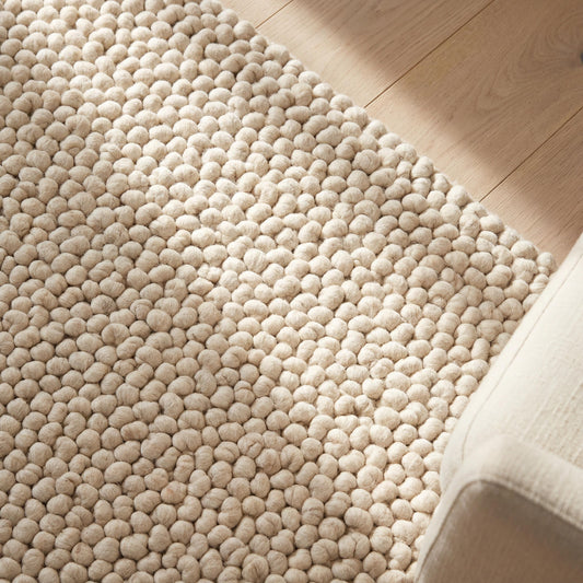 Handmade chunky wool pom pom rug in neutral tones, soft textured area rug for cozy boho nursery and living room decor