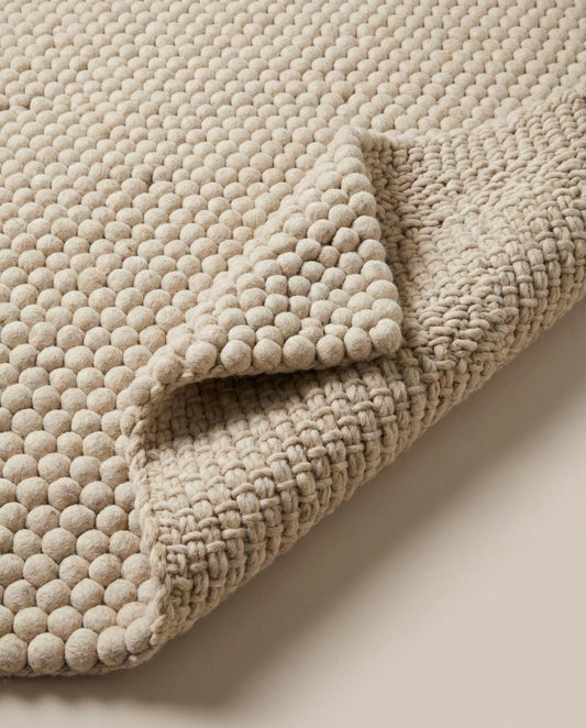 Handmade chunky wool pom pom rug in neutral tones for cozy boho nursery or living room decor
