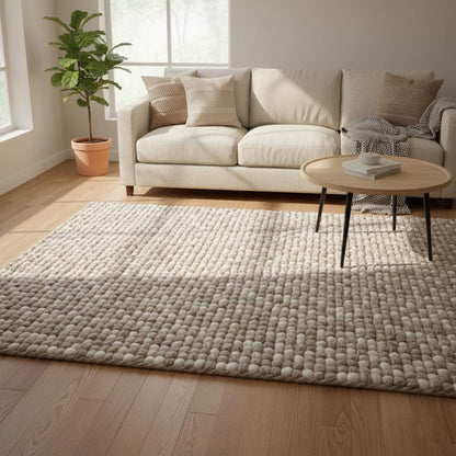 Handwoven chunky wool rug in neutral cream and beige tones with thick felted texture laying on wooden floor.