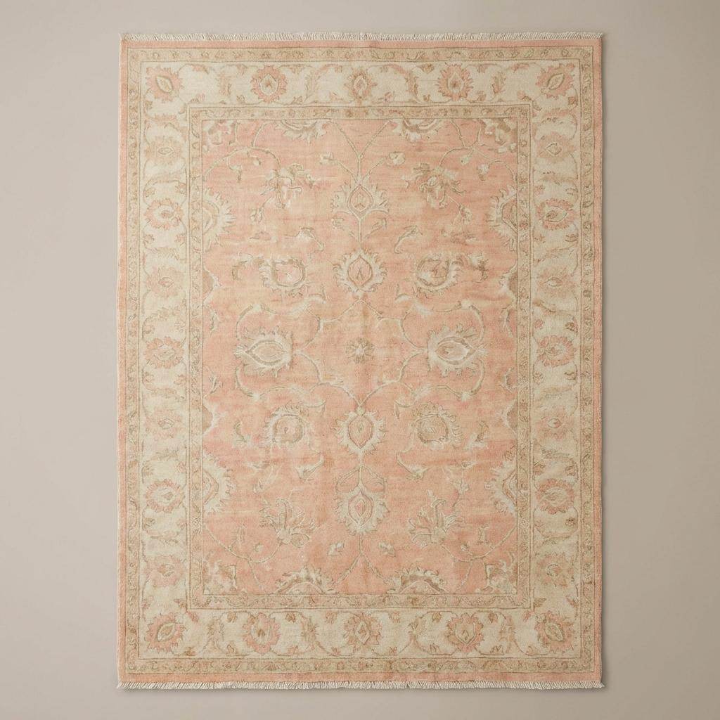 Traditional Persian-style floral vine area rug with muted sage and cream accents on warm wood flooring beside modern chair.