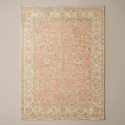 Traditional Persian-style floral vine area rug with muted sage and cream accents on warm wood flooring beside modern chair.