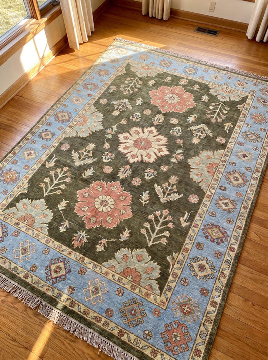 Hand knotted Oushak rug featuring olive green field, floral medallions, and sky blue border displayed in a bright living space __etsy:8122486083