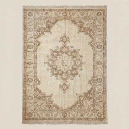 Traditional neutral beige handmade wool area rug with floral border and central medallion placed on dark wooden floor.