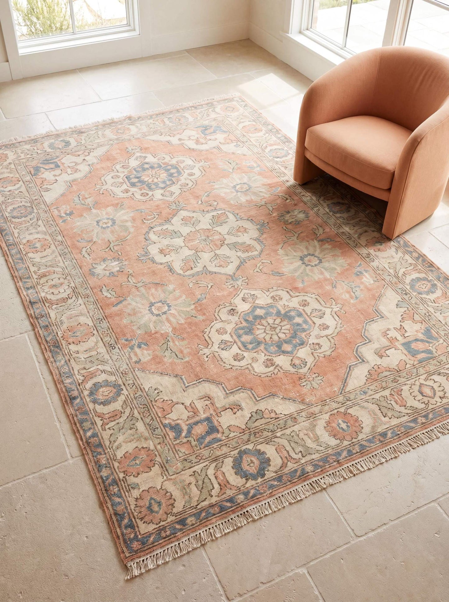 Hand knotted Oushak rug with peach floral medallion design placed in a bright neutral living room beside a curved accent chair __etsy:8099831121