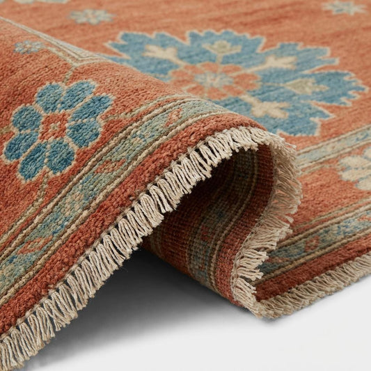 Close up of hand knotted wool pile texture showing individual knots and natural fiber variations in burnt orange and blue wool.