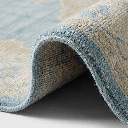 Close up of hand knotted wool rug showing dense individual knots, soft wool pile texture and intricate medallion detailing in blue and beige tones