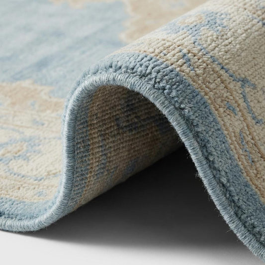 Close up of hand knotted wool rug showing dense individual knots, soft wool pile texture and intricate medallion detailing in blue and beige tones