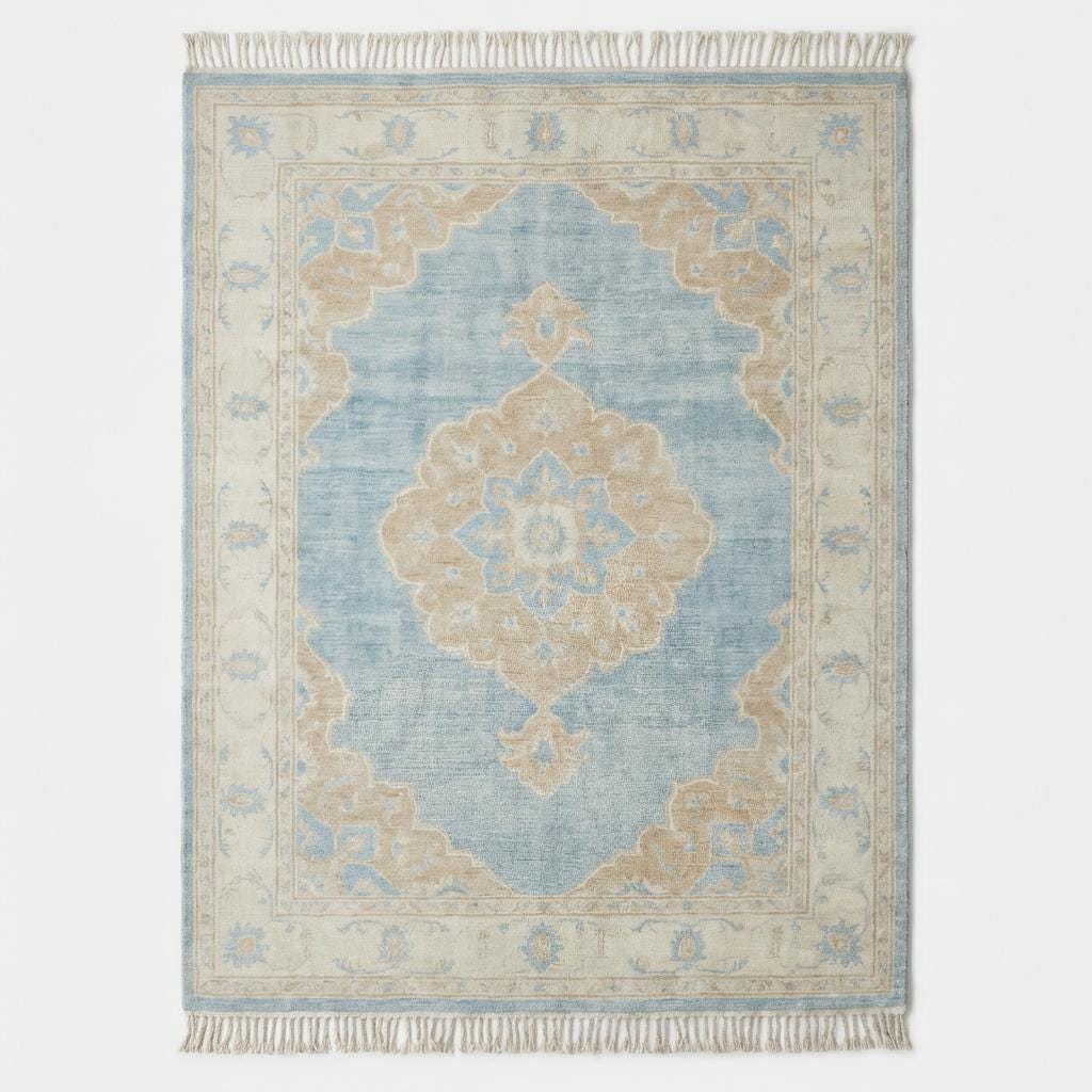 Large blue wool area rug with ivory border and floral medallion placed on light wood flooring beside modern curved sofa