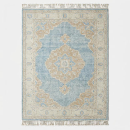 Large blue wool area rug with ivory border and floral medallion placed on light wood flooring beside modern curved sofa