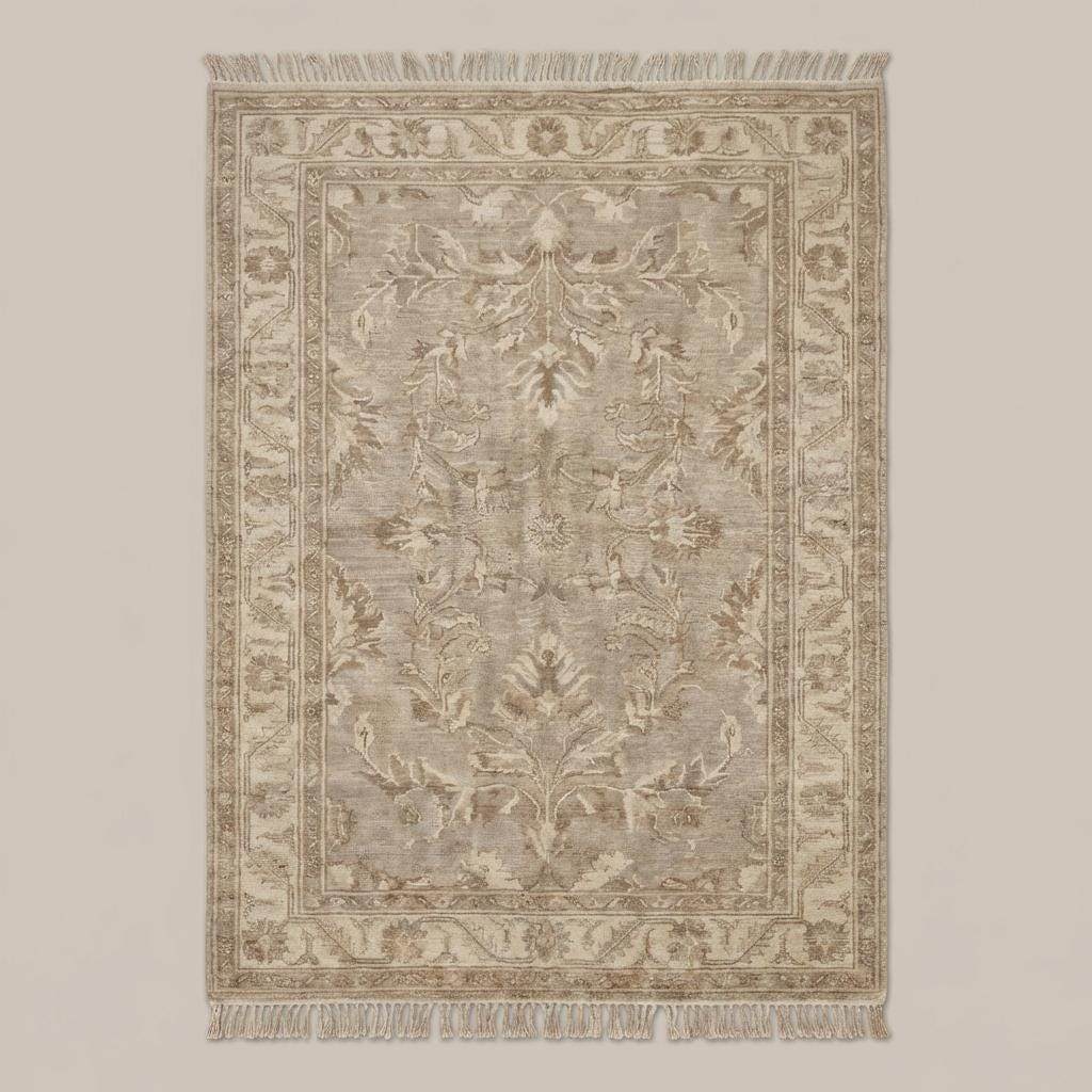 Neutral vintage Persian inspired area rug with decorative border and fringe styled on wooden floor beside chair and pottery