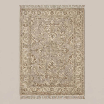 Neutral vintage Persian inspired area rug with decorative border and fringe styled on wooden floor beside chair and pottery