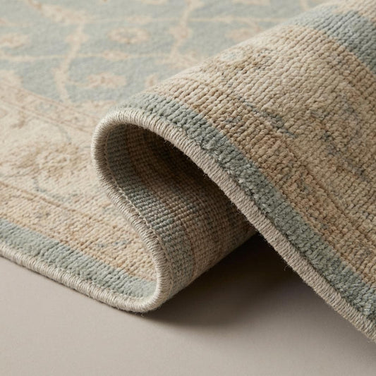 Close-up of hand knotted wool rug showing dense individual knot structure, soft wool fibers, and subtle tonal variation in blue and beige field
