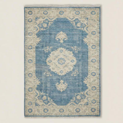 Rectangular blue medallion area rug with traditional Turkish Oushak pattern on light wood floor beside sofa