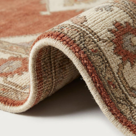 Close up of hand knotted wool pile texture showing individual knots, rich terracotta dye variation, and durable cotton fringe detail.