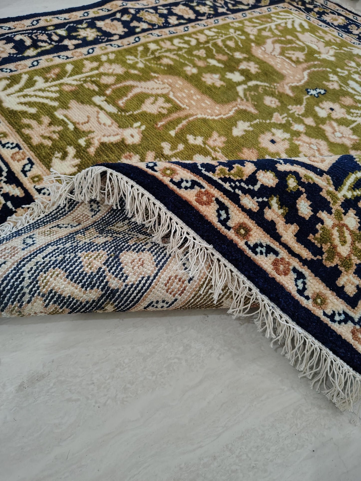 Hand knotted wool rug with green Persian animal design and navy floral border