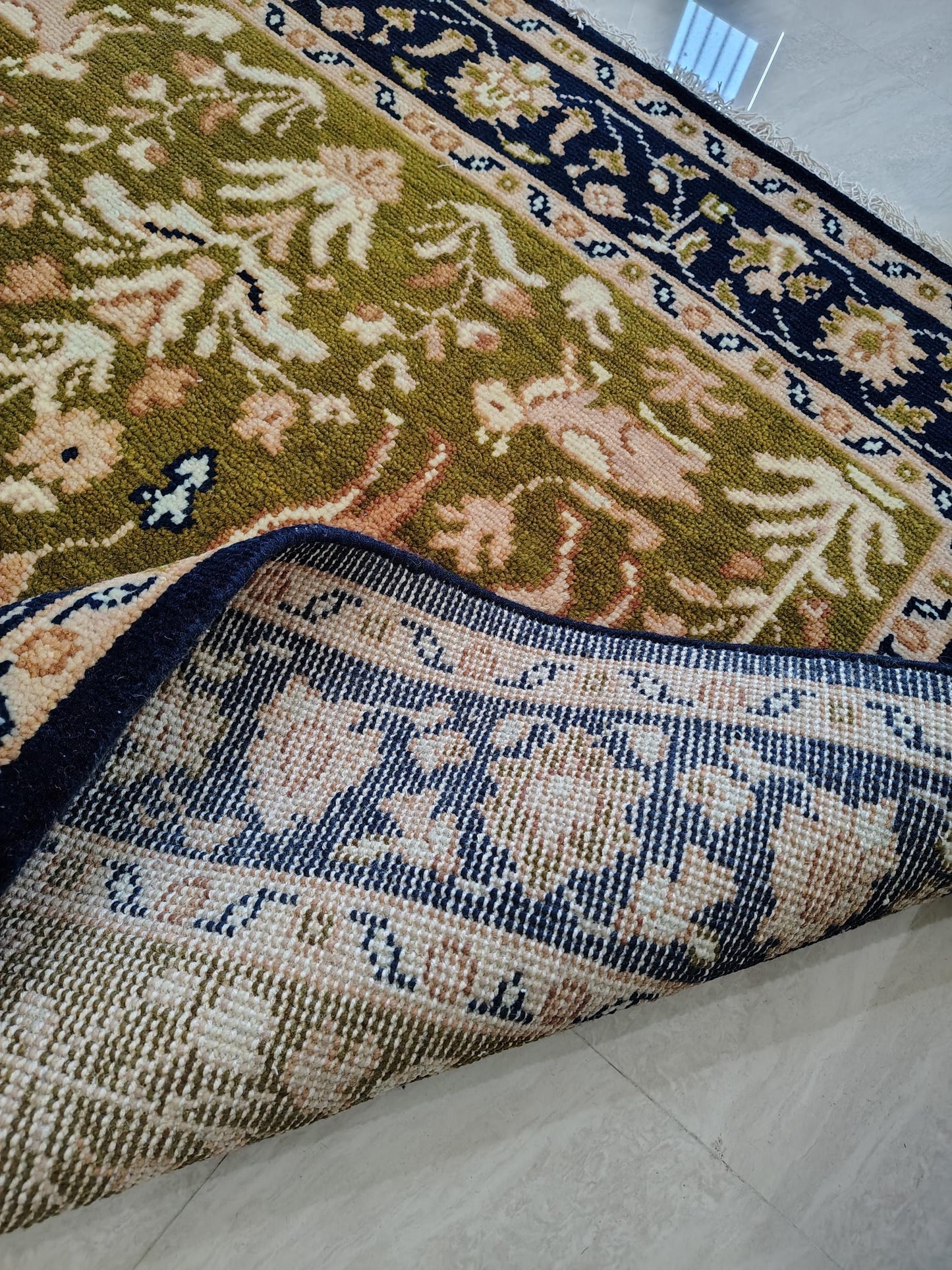 Hand knotted wool rug with Persian animal motifs and navy floral border on olive green field