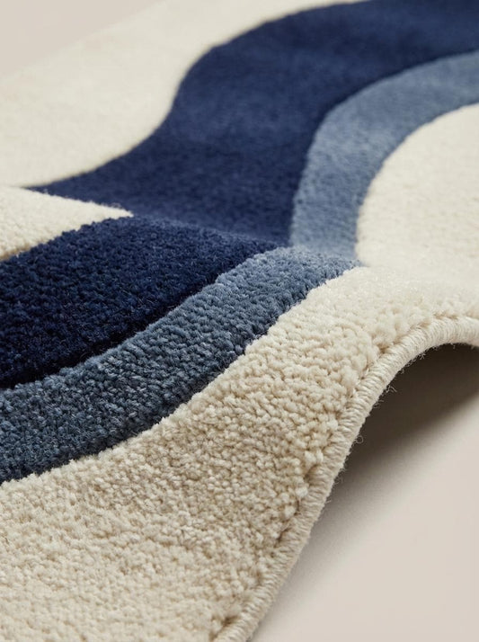 Close up of dense hand tufted wool pile showing soft cut-pile texture and carved wave pattern detailing in navy and slate blue fibers.